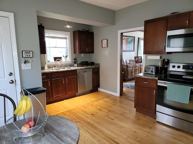 kitchen featuring light wood-style flooring, appliances with stainless steel finishes, baseboards, and a sink