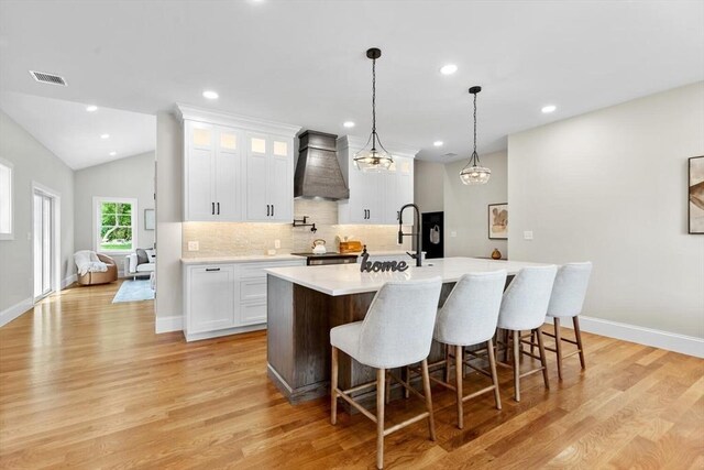 28 Marlboro Rd, Woburn, MA 01801 - kitchen with custom exhaust hood, a center island with sink, light countertops, decorative backsplash, and light wood finished floors