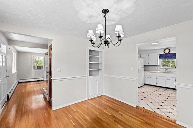 32 Gannett Pasture Ln, Scituate, MA 02066 - unfurnished dining area featuring baseboard heating, a chandelier, cooling unit, light wood finished floors, and a textured ceiling