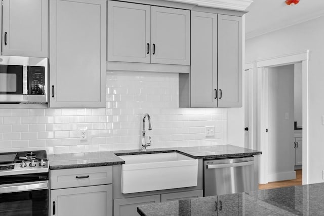 kitchen with appliances with stainless steel finishes, backsplash, dark stone counters, and sink