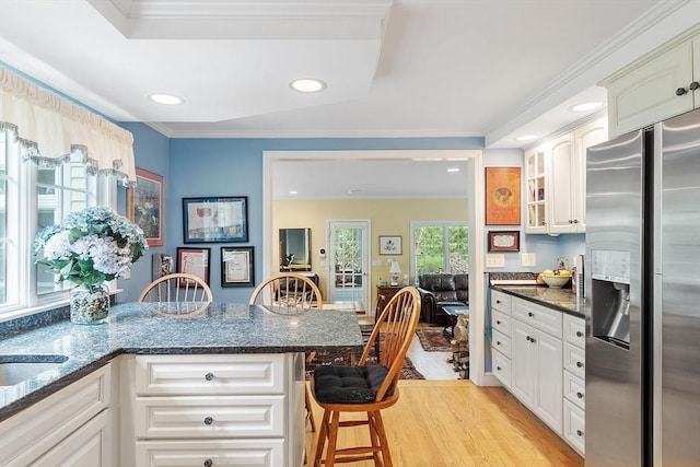 kitchen with stainless steel refrigerator with ice dispenser, light wood-style flooring, a breakfast bar area, recessed lighting, and glass insert cabinets