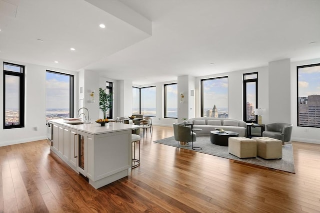 kitchen featuring a kitchen bar, sink, a center island with sink, hardwood / wood-style floors, and white cabinets