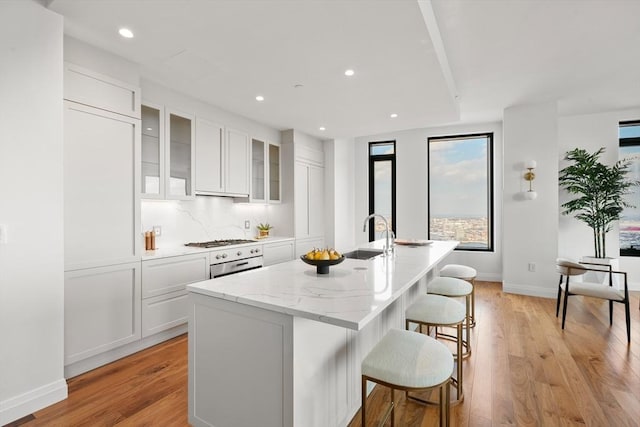 kitchen with sink, a center island with sink, light wood-type flooring, a kitchen breakfast bar, and white cabinets