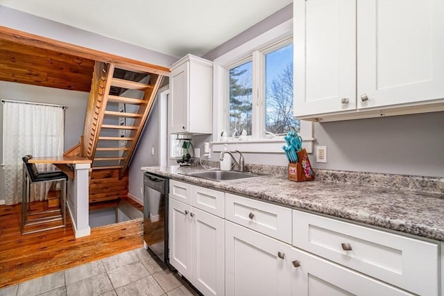 kitchen featuring dishwashing machine, sink, white cabinets, and light stone counters