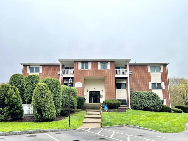 view of front of property with brick siding, uncovered parking, and a front lawn