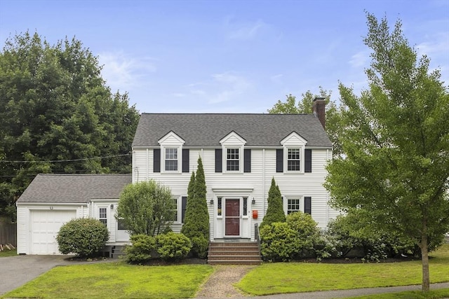 colonial inspired home with a chimney, an attached garage, driveway, and a front yard