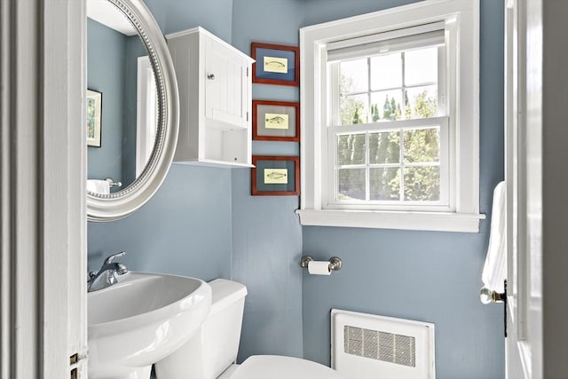 bathroom featuring toilet, heating unit, and a sink