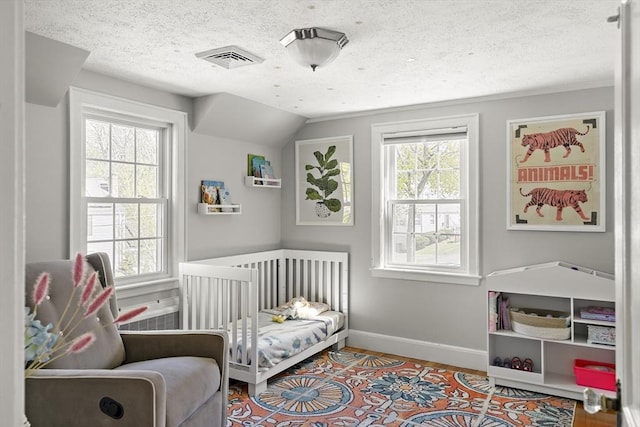 bedroom featuring a textured ceiling, visible vents, wood finished floors, baseboards, and lofted ceiling