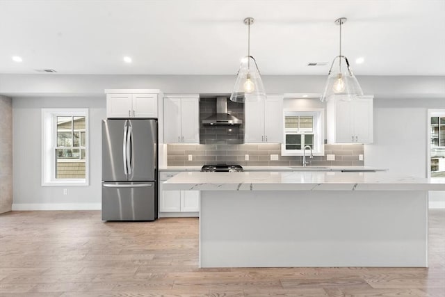 kitchen featuring light wood finished floors, white cabinets, freestanding refrigerator, wall chimney range hood, and backsplash