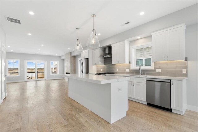 kitchen with light wood finished floors, visible vents, wall chimney exhaust hood, appliances with stainless steel finishes, and a sink