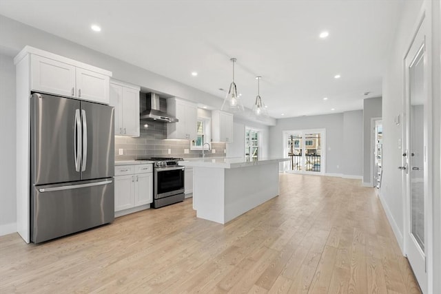 kitchen featuring light countertops, backsplash, appliances with stainless steel finishes, white cabinetry, and wall chimney range hood