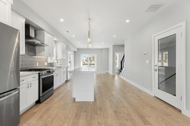 kitchen with wall chimney exhaust hood, a sink, stainless steel appliances, light wood-type flooring, and backsplash