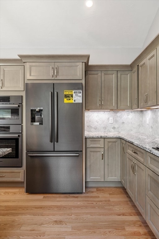 kitchen featuring tasteful backsplash, light hardwood / wood-style flooring, light stone counters, lofted ceiling, and appliances with stainless steel finishes