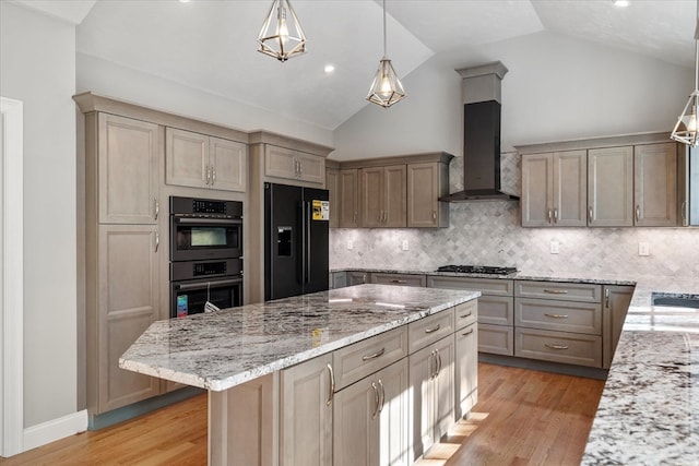 kitchen with a kitchen island, light stone countertops, light wood-type flooring, stainless steel appliances, and wall chimney range hood