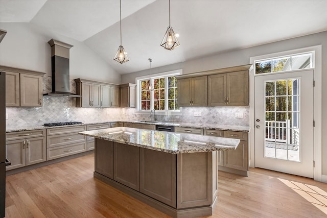 kitchen featuring pendant lighting, wall chimney range hood, a center island, and a wealth of natural light