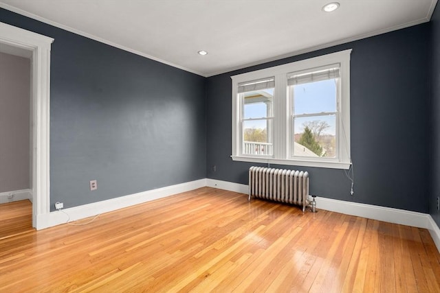 empty room featuring crown molding, hardwood / wood-style flooring, baseboards, and radiator heating unit