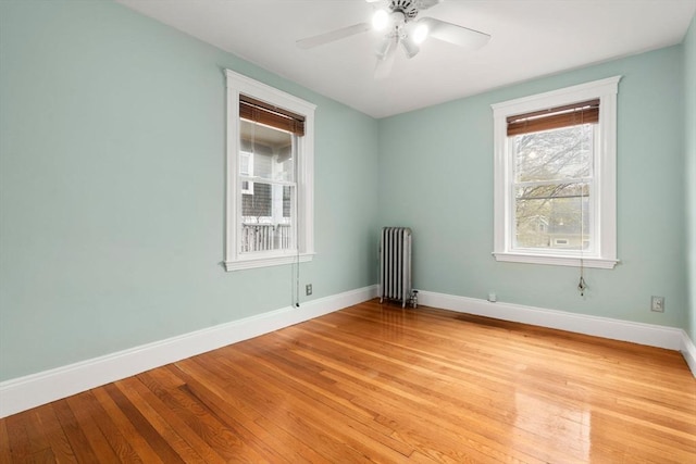unfurnished room featuring light wood-style floors, baseboards, a ceiling fan, and radiator heating unit
