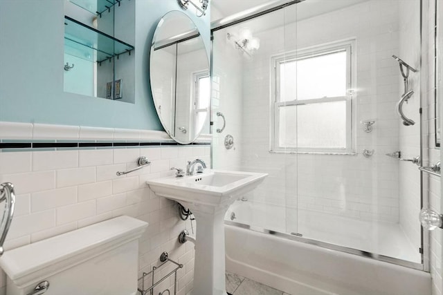 bathroom with tile walls, toilet, and combined bath / shower with glass door