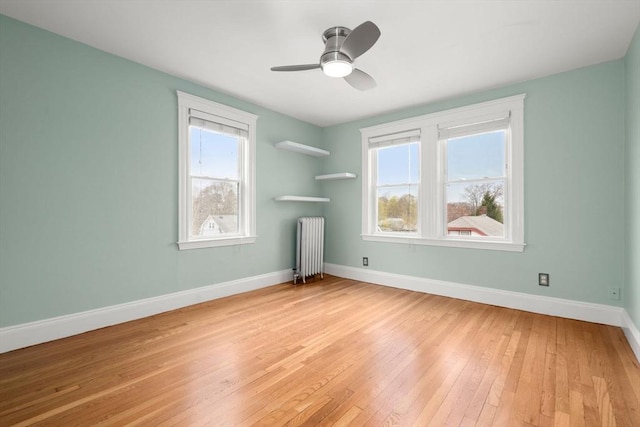 unfurnished room with light wood-style floors, baseboards, a ceiling fan, and radiator heating unit