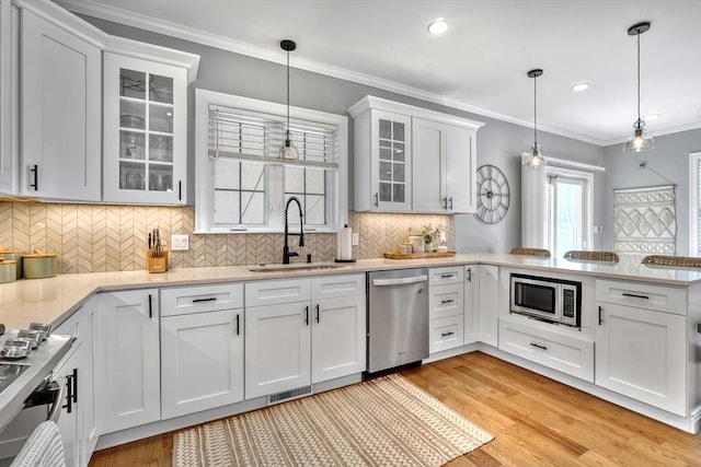 kitchen with appliances with stainless steel finishes, white cabinetry, sink, hanging light fixtures, and crown molding