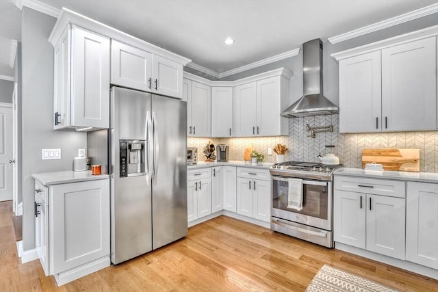 kitchen with wall chimney range hood, appliances with stainless steel finishes, ornamental molding, light hardwood / wood-style floors, and white cabinets