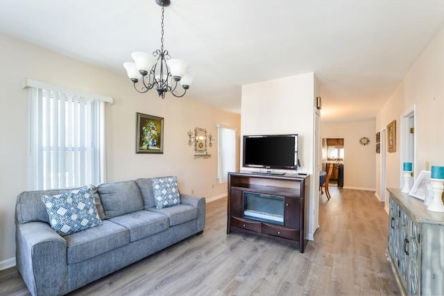 living room with a notable chandelier, light wood-style flooring, and baseboards