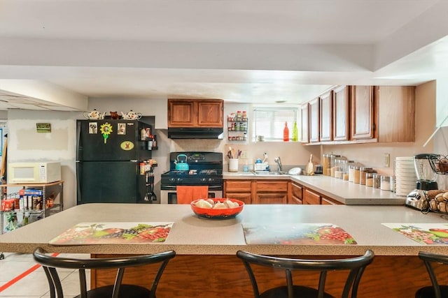 kitchen with white microwave, freestanding refrigerator, light countertops, under cabinet range hood, and gas range