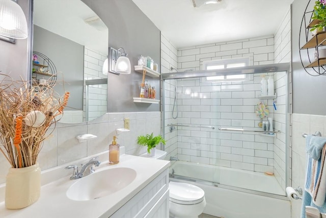 full bathroom with toilet, vanity, wainscoting, combined bath / shower with glass door, and tile walls