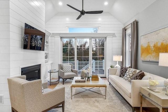 living room featuring ceiling fan, wood walls, and lofted ceiling