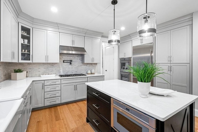 kitchen featuring a kitchen island, decorative light fixtures, built in appliances, decorative backsplash, and light hardwood / wood-style flooring