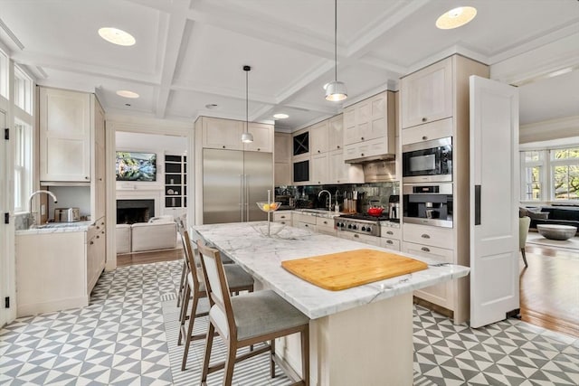 kitchen featuring light flooring, a breakfast bar, built in appliances, coffered ceiling, and light stone countertops