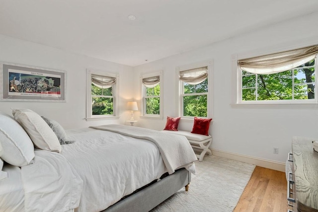 bedroom with multiple windows, wood finished floors, and baseboards