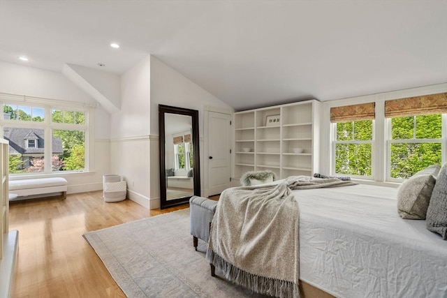 bedroom with wood finished floors, vaulted ceiling, and a wainscoted wall