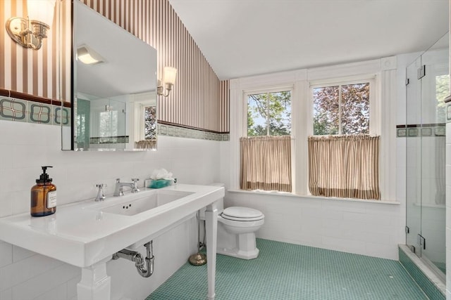 bathroom featuring tile walls, a stall shower, wallpapered walls, toilet, and a sink