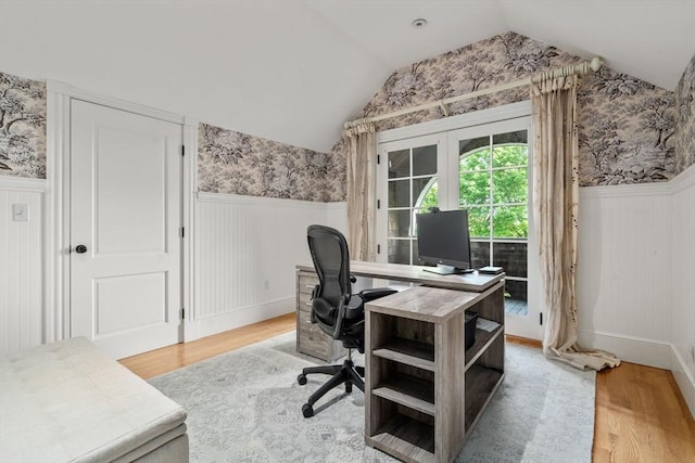 office space featuring wallpapered walls, light wood-type flooring, lofted ceiling, and a wainscoted wall