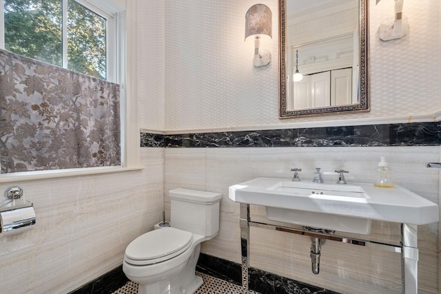 half bath featuring wallpapered walls, toilet, wainscoting, and tile walls