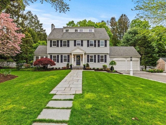 colonial inspired home featuring an attached garage, driveway, a front yard, and a chimney