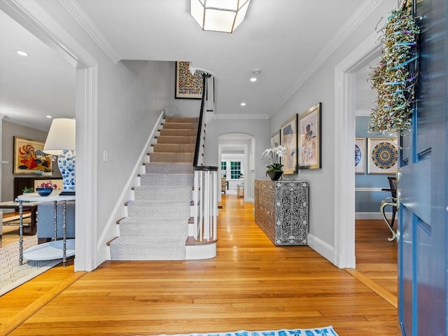 foyer with stairs, arched walkways, wood-type flooring, crown molding, and baseboards