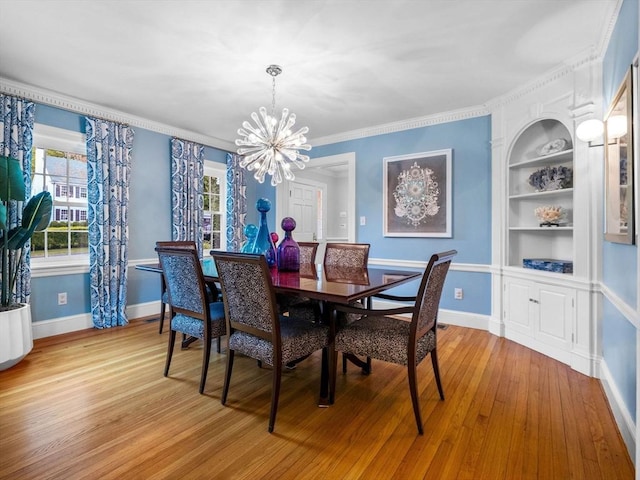 dining space featuring a chandelier, light wood-style flooring, built in shelves, baseboards, and crown molding