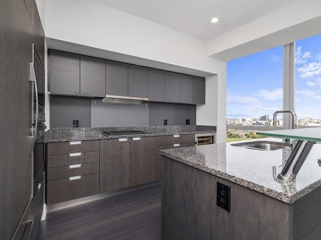 kitchen with sink, dark wood-type flooring, light stone countertops, stainless steel gas cooktop, and an island with sink