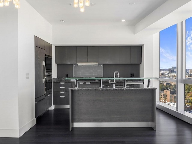 kitchen with backsplash, dark wood-type flooring, exhaust hood, and dark stone counters