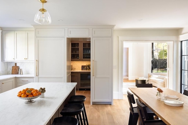 kitchen with a breakfast bar, pendant lighting, decorative backsplash, glass insert cabinets, and light wood-type flooring