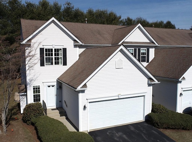 traditional home with aphalt driveway, a garage, and a shingled roof