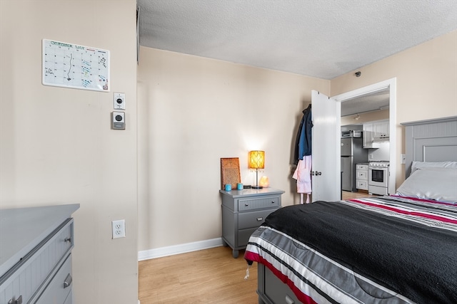 bedroom with stainless steel fridge, light wood-type flooring, and a textured ceiling