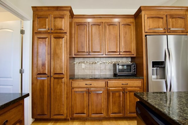 kitchen with dark stone counters, a toaster, stainless steel fridge with ice dispenser, and backsplash