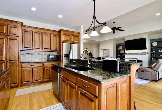 kitchen with a sink, open floor plan, dark stone counters, appliances with stainless steel finishes, and light wood finished floors