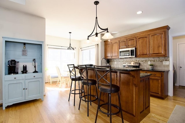 kitchen with light wood-style flooring, stainless steel microwave, a kitchen breakfast bar, backsplash, and brown cabinetry