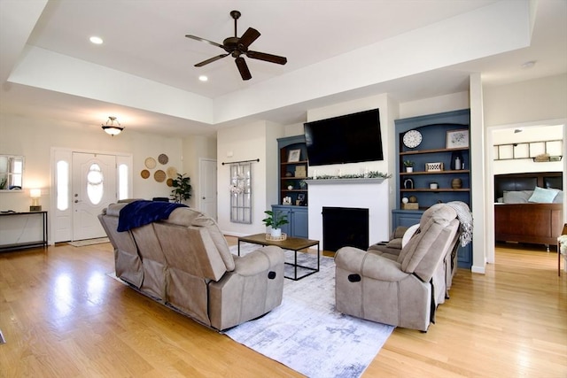 living area with built in features, light wood-style flooring, a fireplace, and a raised ceiling