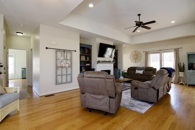 living room featuring visible vents, baseboards, a tray ceiling, a fireplace, and light wood-style floors