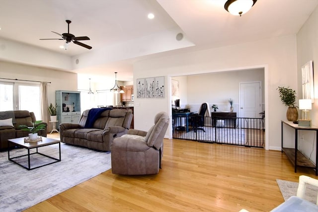 living area featuring a tray ceiling, ceiling fan with notable chandelier, baseboards, and light wood finished floors